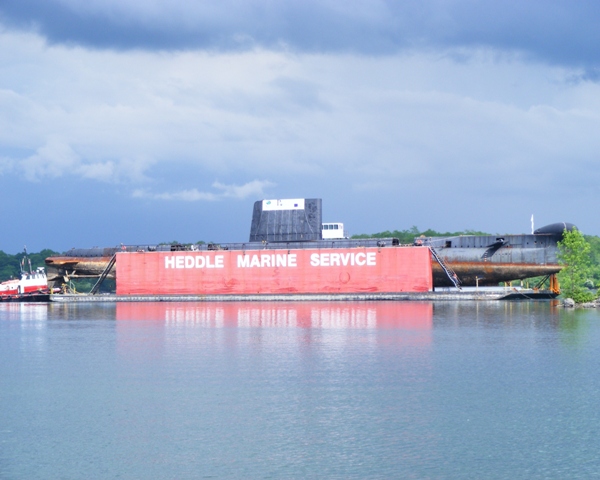 HMCS OJIBWA under tow in the St. Lawrence river approaching the seaway lock at Iroquois, Ontario on 3 June 2012. loaded onto the Heddle Marine barge in Halifax, the cold war RCN submarine is being moved to Port Burwell to become a museum ship.

Roger Litwiller Collection, courtesy Alex Litwiller (AJL DSCF9649)