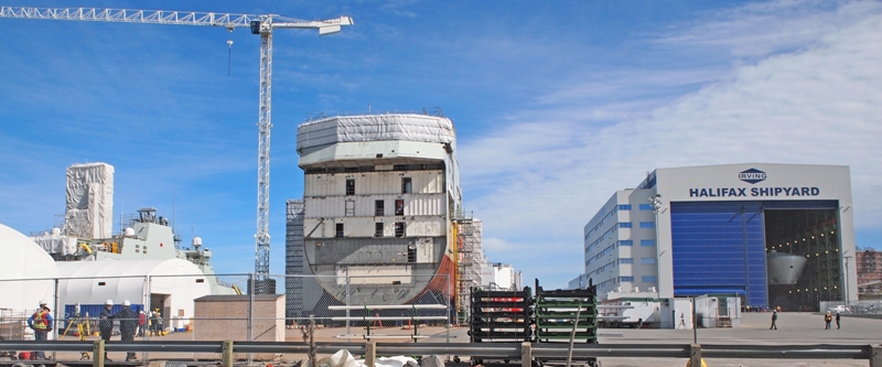 Irving Shipyard in Halifax is a buzz of activity on 3 May 2018 as the bow mega-block for the future HMCS MARGARET BROOKE is being prepared to leave the Assembly Hall and join the Arctic and Offshore Patrol Ship in the centre of the photo. to the left of MARGARET BROOKE is the the future HMCS HARRY DEWOLF already in the water and finishing construction for her transfer to the RCN later in the year. Roger Litwiller Collection, courtesy Roger Litwiller. (RTL39612)