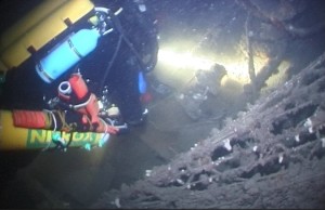 A second screenshot from the same video showing an unidentified diver securing a recovery bag to the Brass lamp. The diver has several of red recovery bags strapped to their dive equipment.